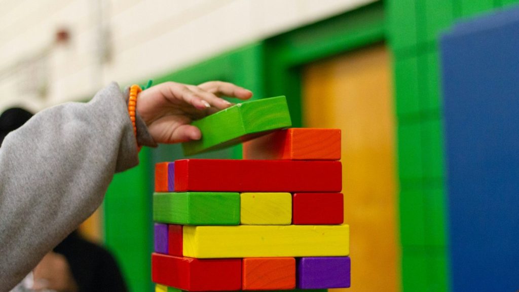 Duas crianças brincando e empilhando blocos coloridos de madeira, simbolizando ludicidade e desenvolvimento emocional