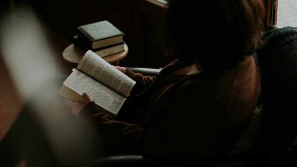 Mulher sentada confortavelmente lendo um livro, em um momento de autocuidado e presença