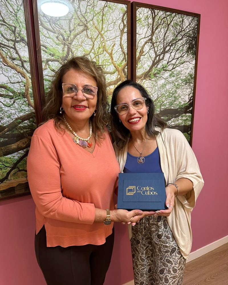 Aletheia Campos e Dora Firmo segurando a caixa do jogo Contos em Cubos